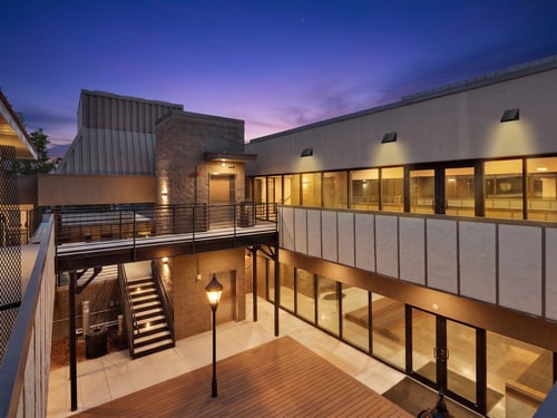 Commercial building courtyard at dusk illuminated by wall-mounted exterior lighting, pathway lights and architectural fixtures.